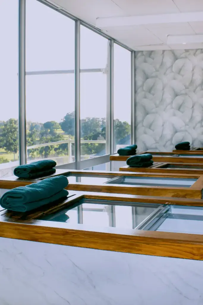 Modern spa pool room with teal towels, wooden deck, panoramic windows overlooking green landscape