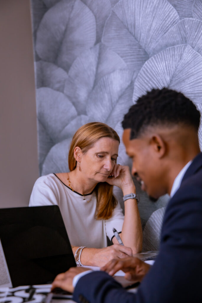 Two professionals collaborating at laptop during business meeting in modern office with floral wall art background.