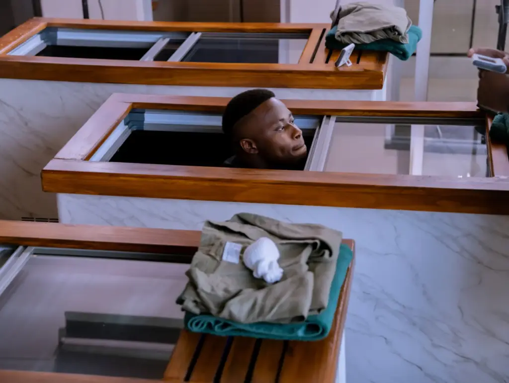 Man peeking out of wooden display case with folded clothes on shelf in minimalist setting