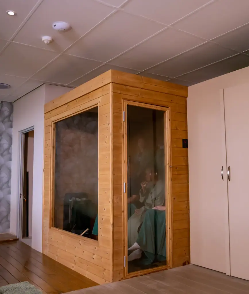 Wooden sauna cabin with glass doors in modern spa facility with pink walls and drop ceiling