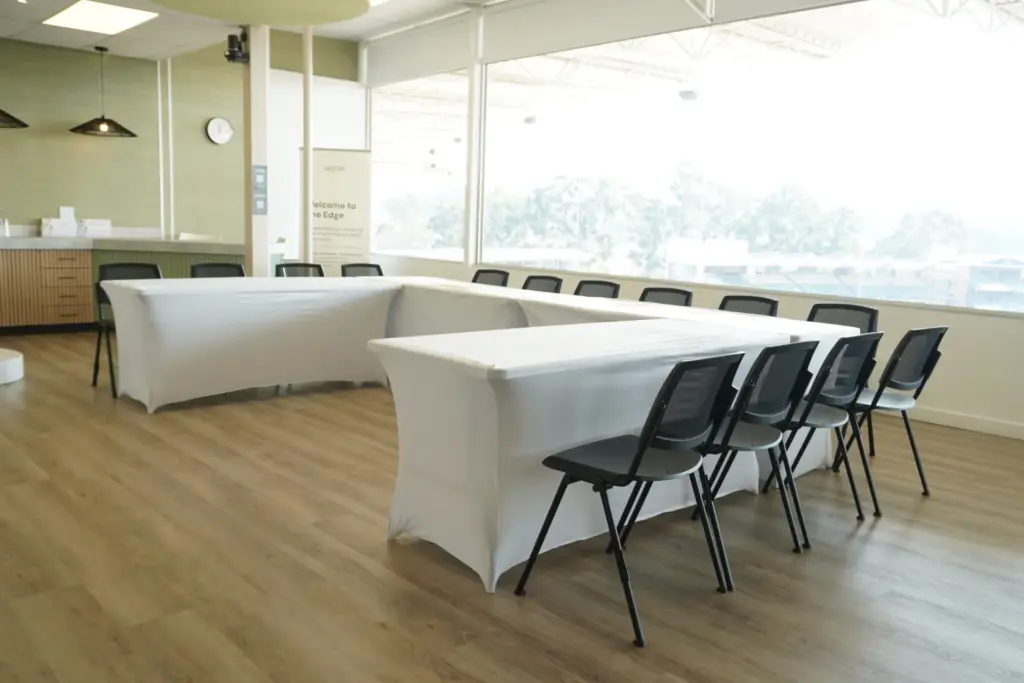 Modern office conference room with white tables, black chairs, and panoramic city views through floor-to-ceiling windows.
