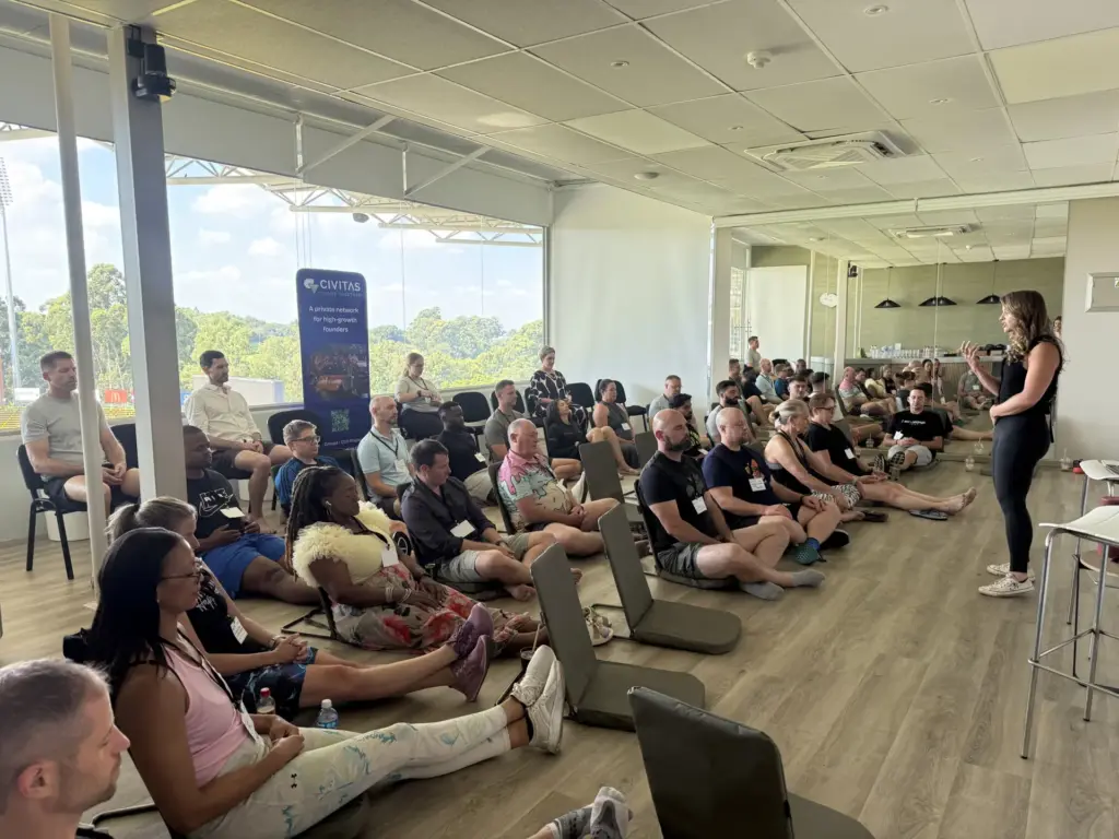 Woman speaking to diverse audience seated on floor in modern office space with CIVITAS banner visible