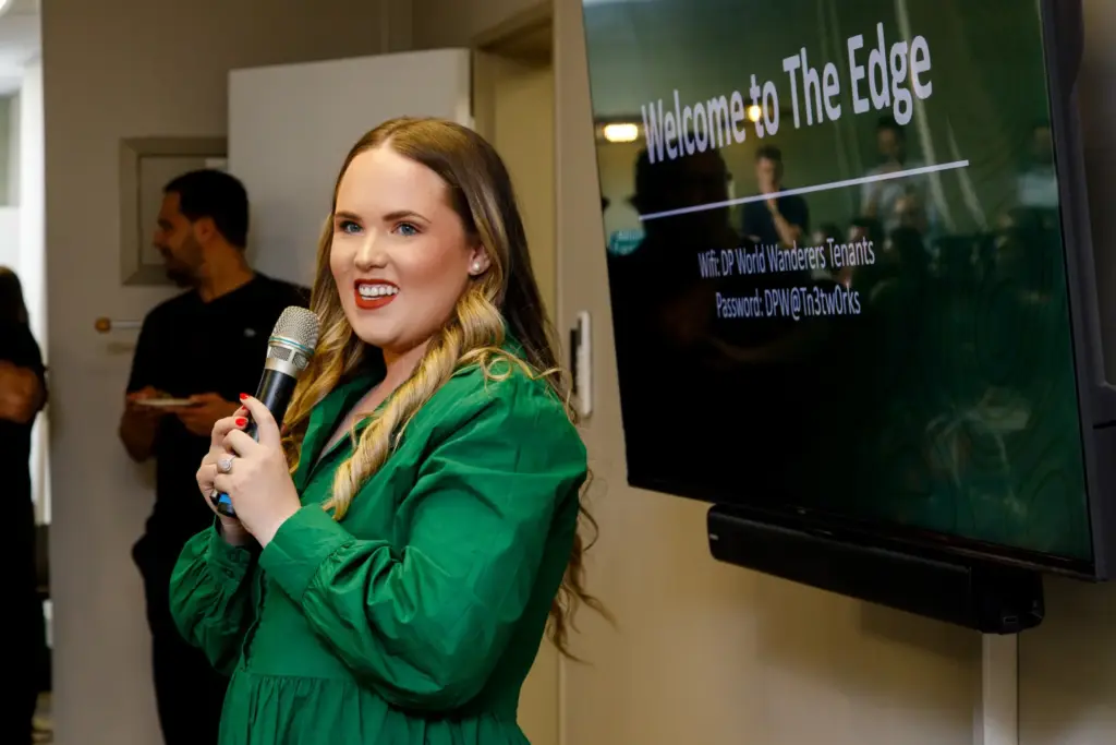 Woman in green blazer speaking at microphone with Welcome to The Edge display screen visible