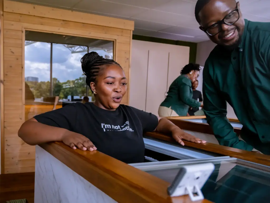 Woman in black shirt interacting with wooden display case while man in green shirt smiles nearby in modern museum interior