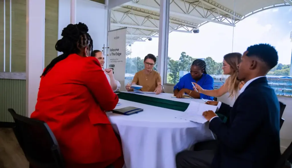 Professional team meeting at modern office with waterfront view, diverse group discussing business strategy around table.