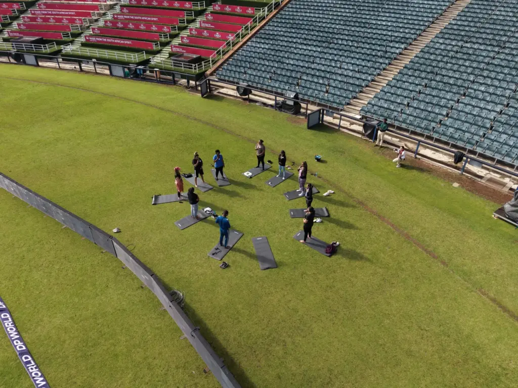 Group fitness class exercising on mats at a large stadium field with empty stands.